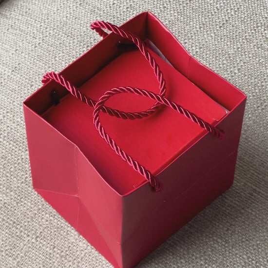 red rose on top of rotating box with gold loveknot necklace